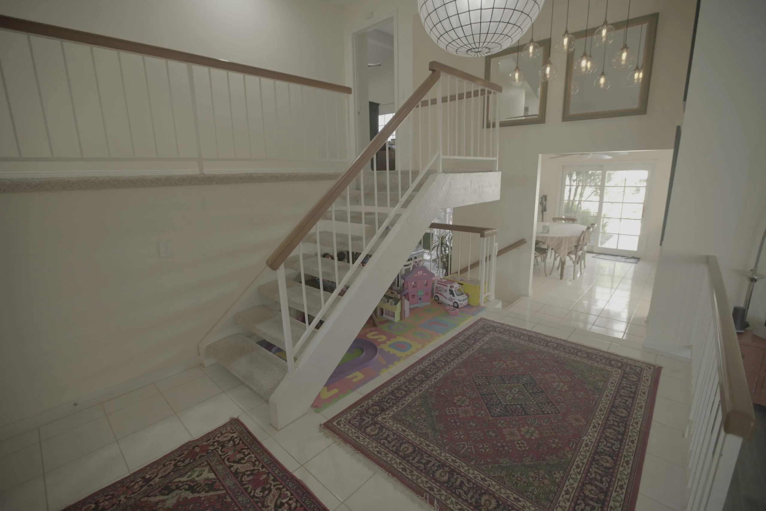A two-story foyer with a white staircase, a patterned rug, and a chandelier