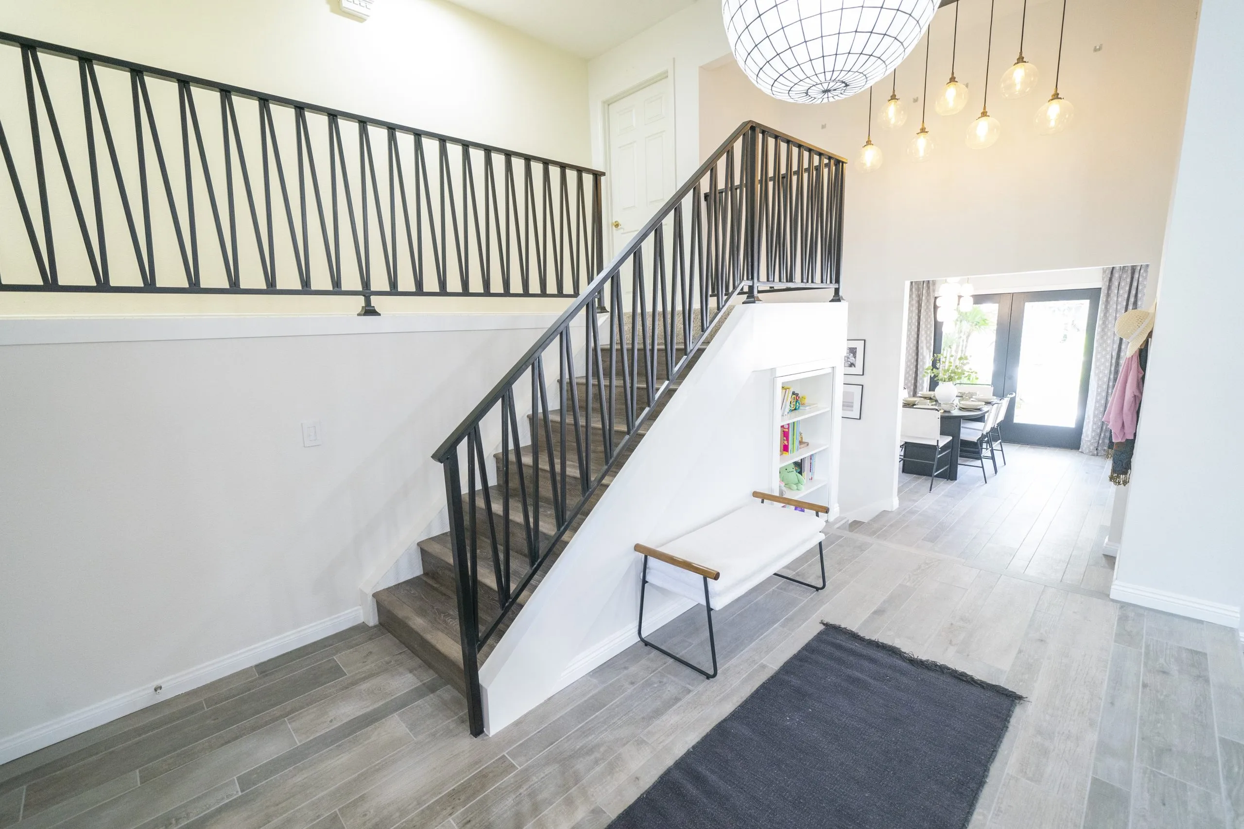 Modern entryway with a black metal staircase, pendant lighting, and open dining area