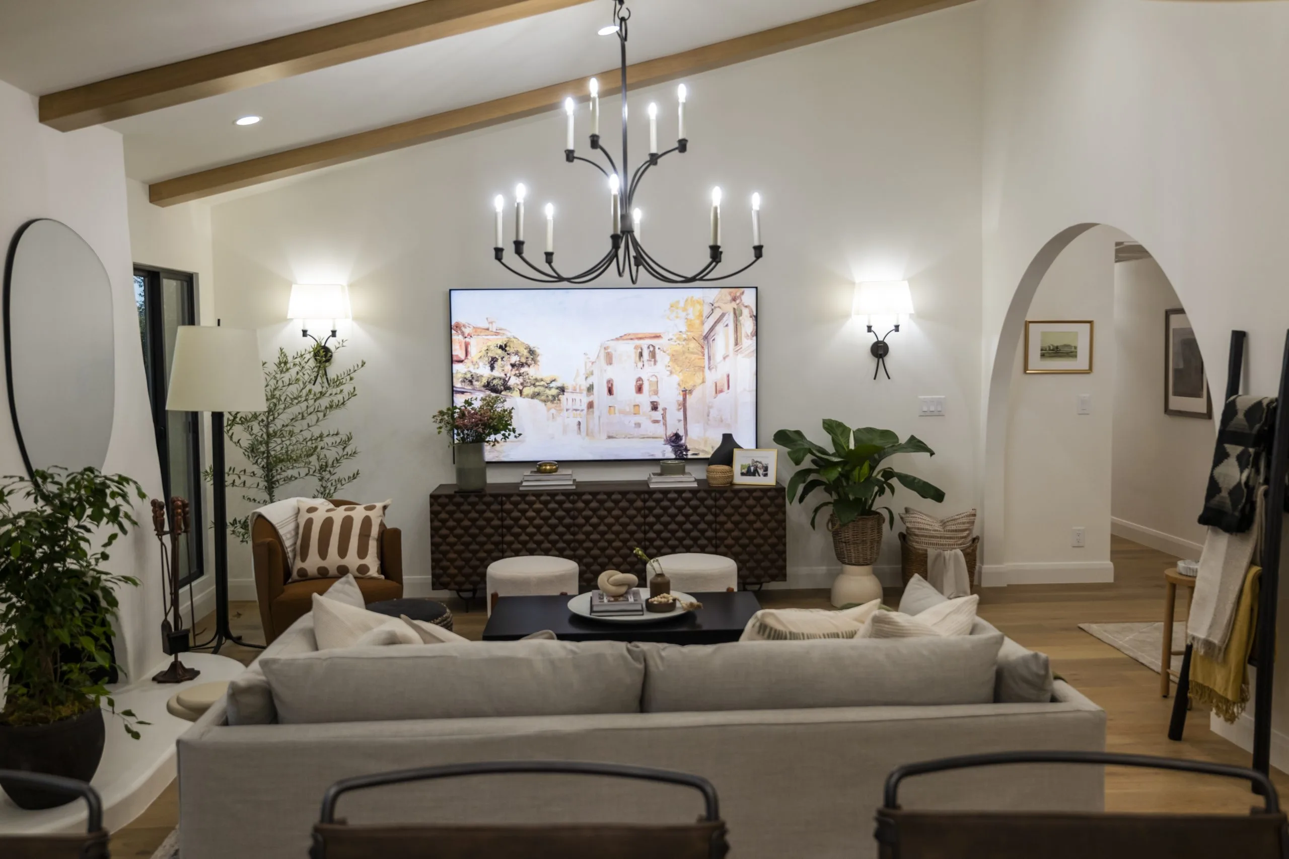 Modern living room with neutral tones, chandelier, arched doorway, and wall-mounted TV